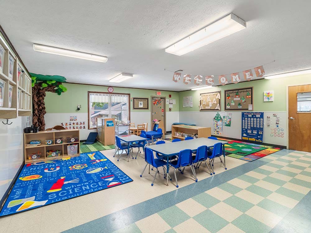 An empty preschool classroom with small tables, chairs, and colorful rugs