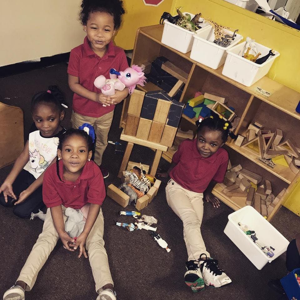 Four children playing on the floor in a room with shelves of toys