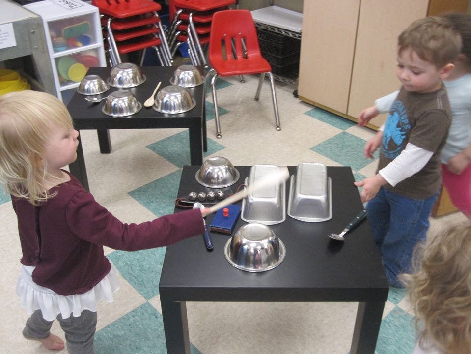 Child playing with metal bowls and a stick on a table