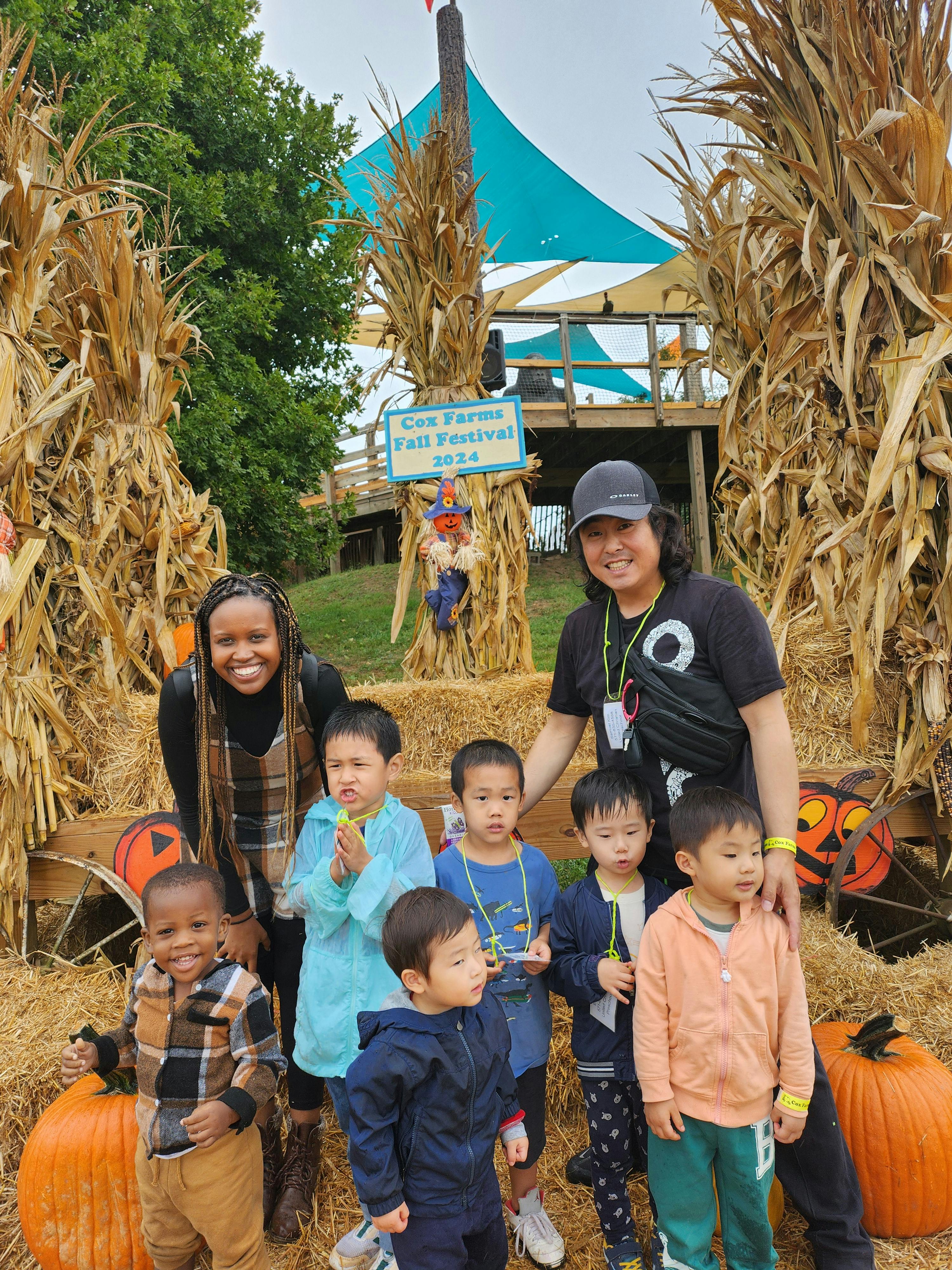 Group of adults and children standing in front of Cox Farms Fall Festival sign