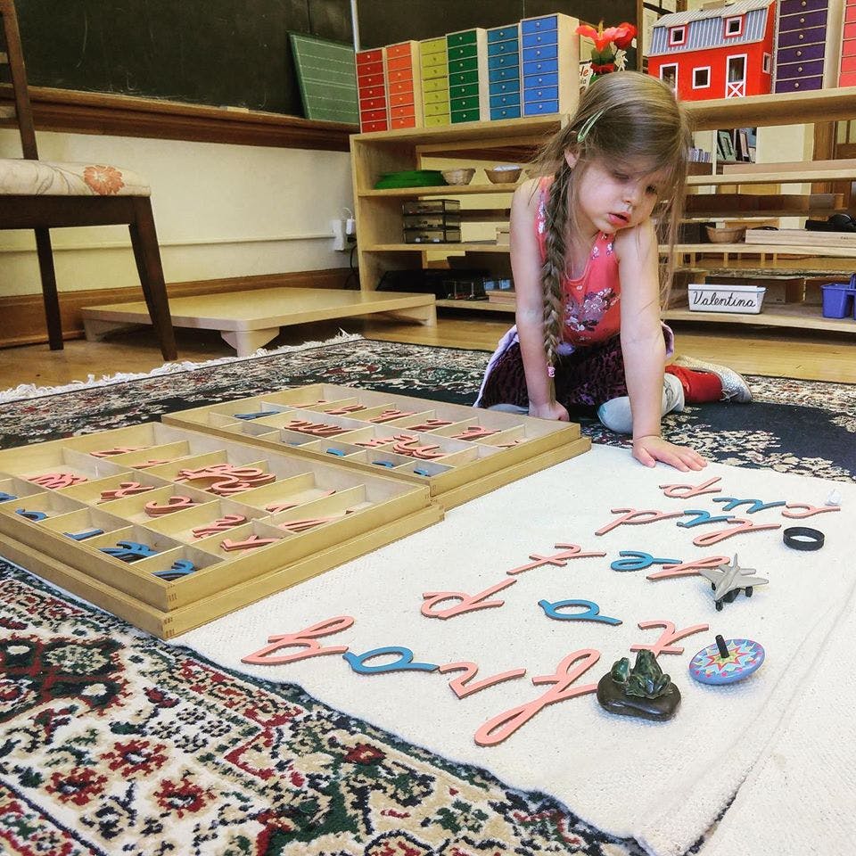 Child on floor arranging letter cutouts on a mat