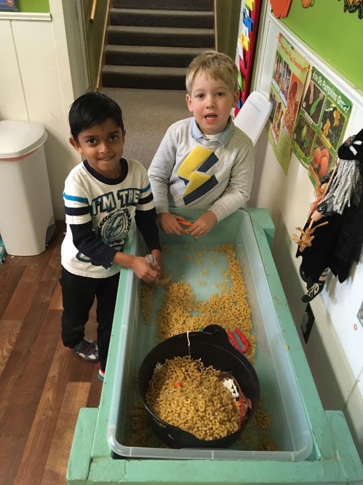 Two children playing with pasta in a sensory bin