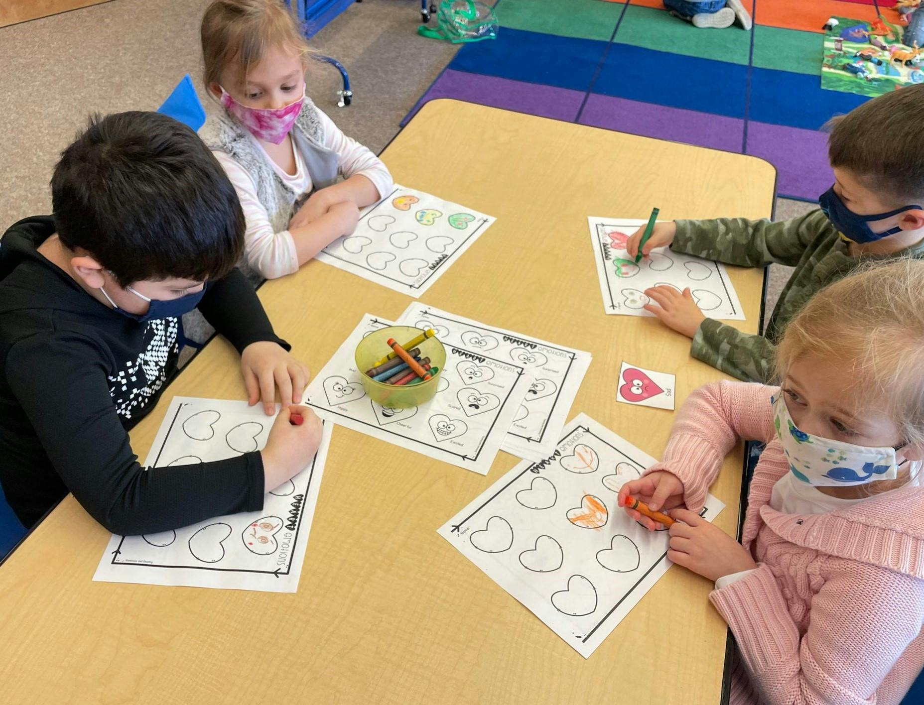 Four children coloring at a table in a classroom