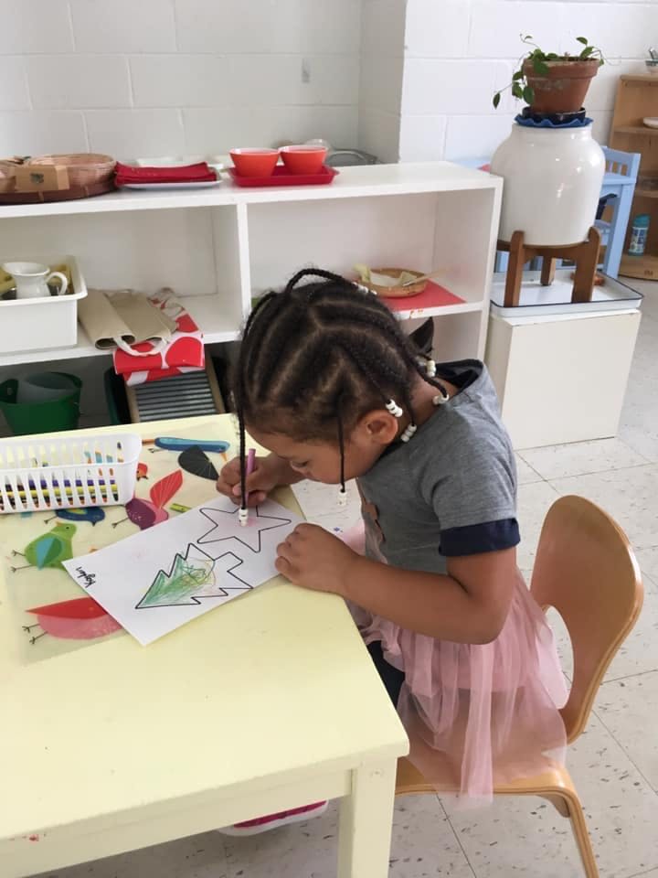 Child coloring a drawing of a Christmas tree and star at a table