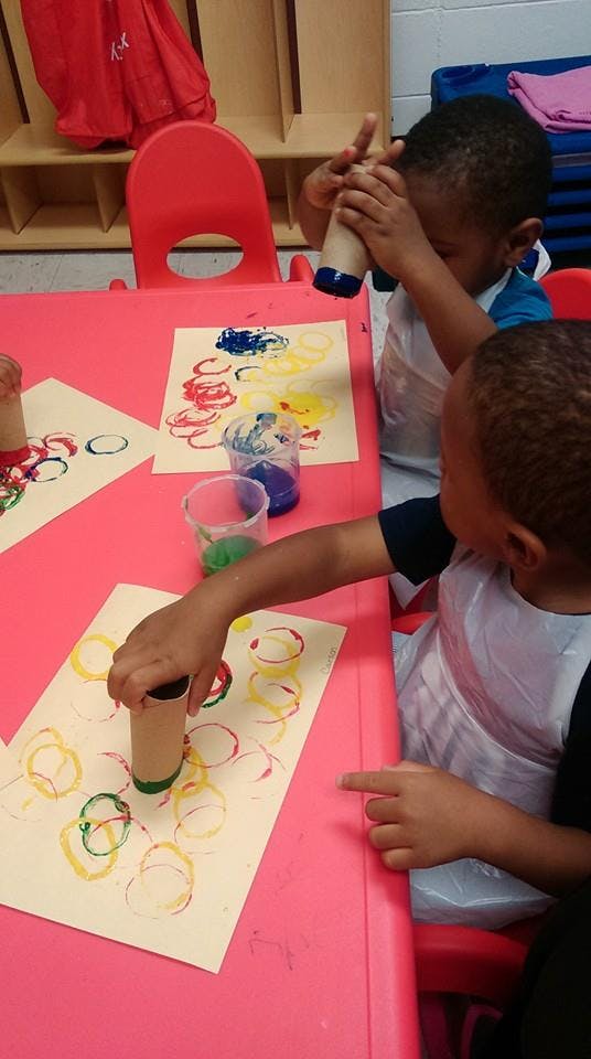 Two children making circle prints with cardboard tubes and paint in a classroom