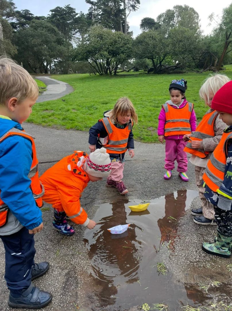 Children playing with paper boats in a puddle