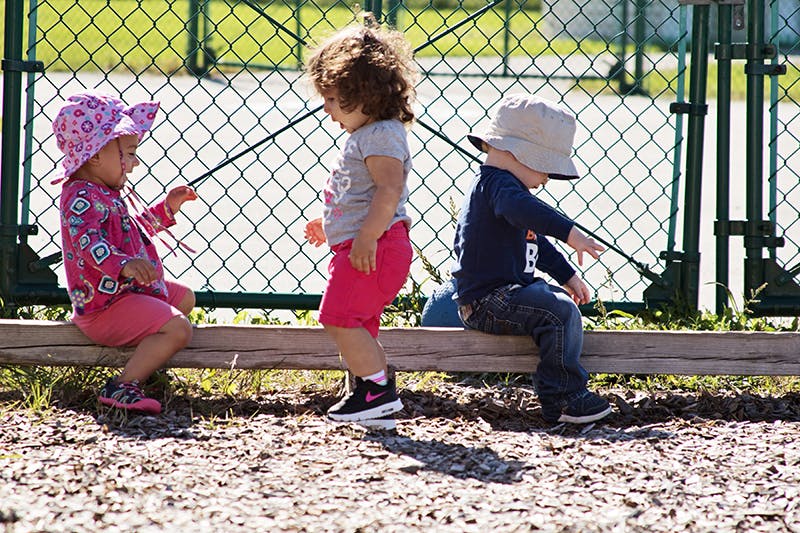 Three children playing outdoors near a fence