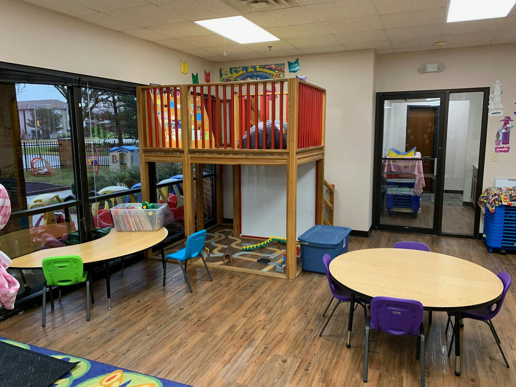 Indoor play area with a two-story play structure and small tables with chairs