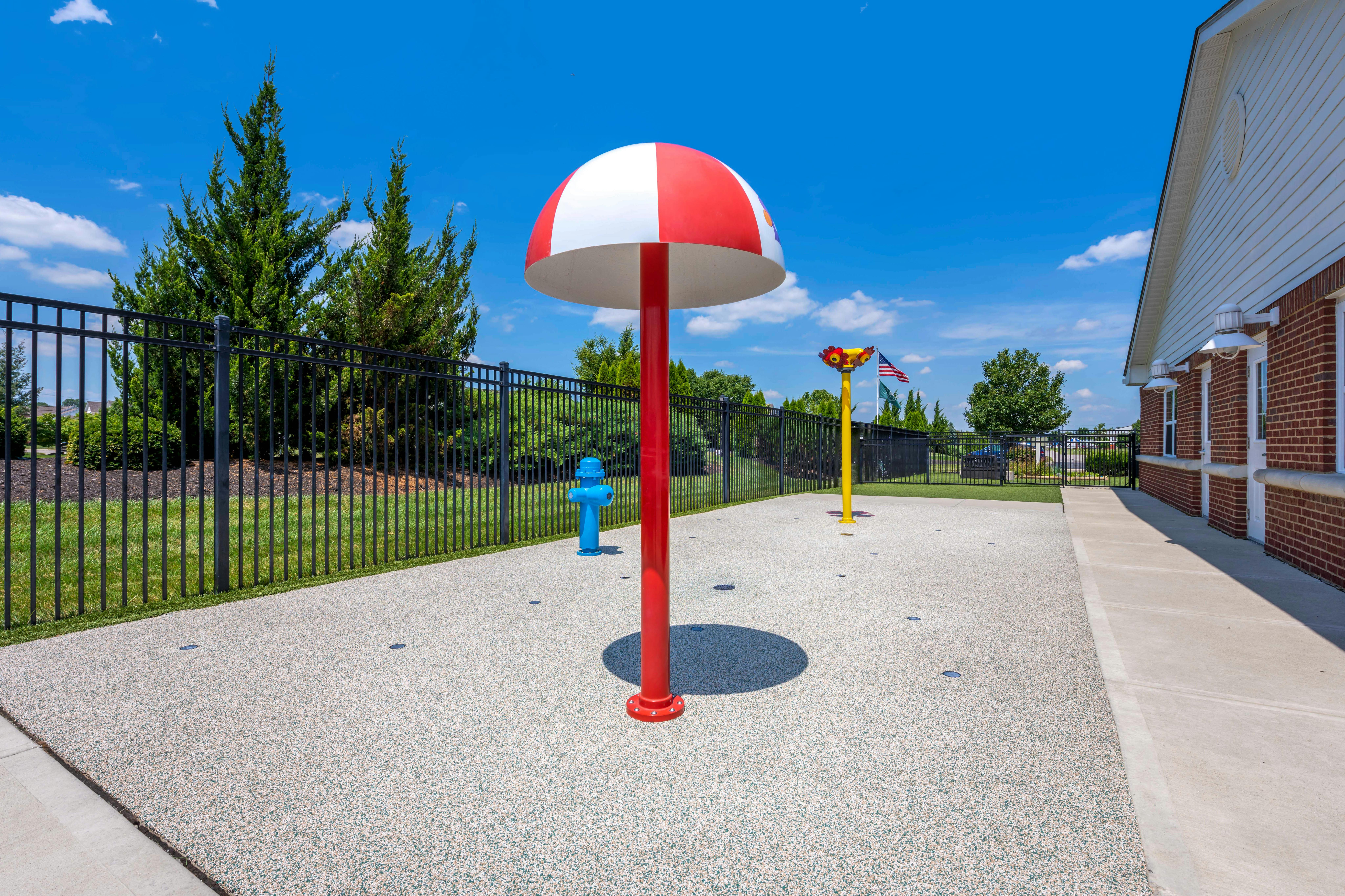 A colorful splash pad with a red and white umbrella, a blue fire hydrant, and a yellow sprinkler