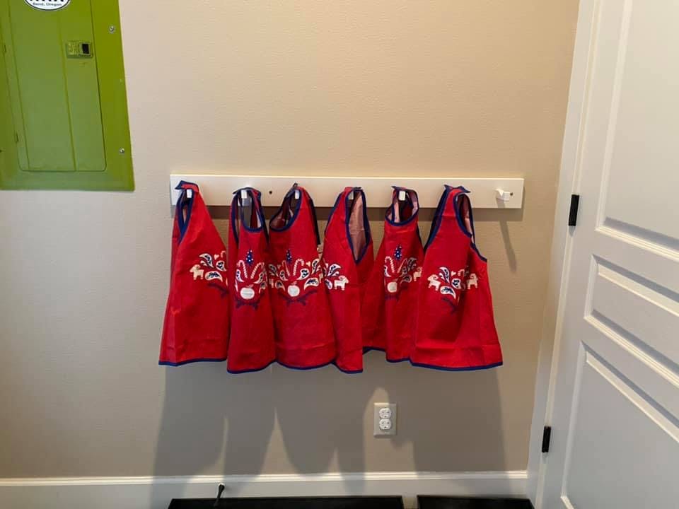 Red aprons with white designs hanging on a wall rack