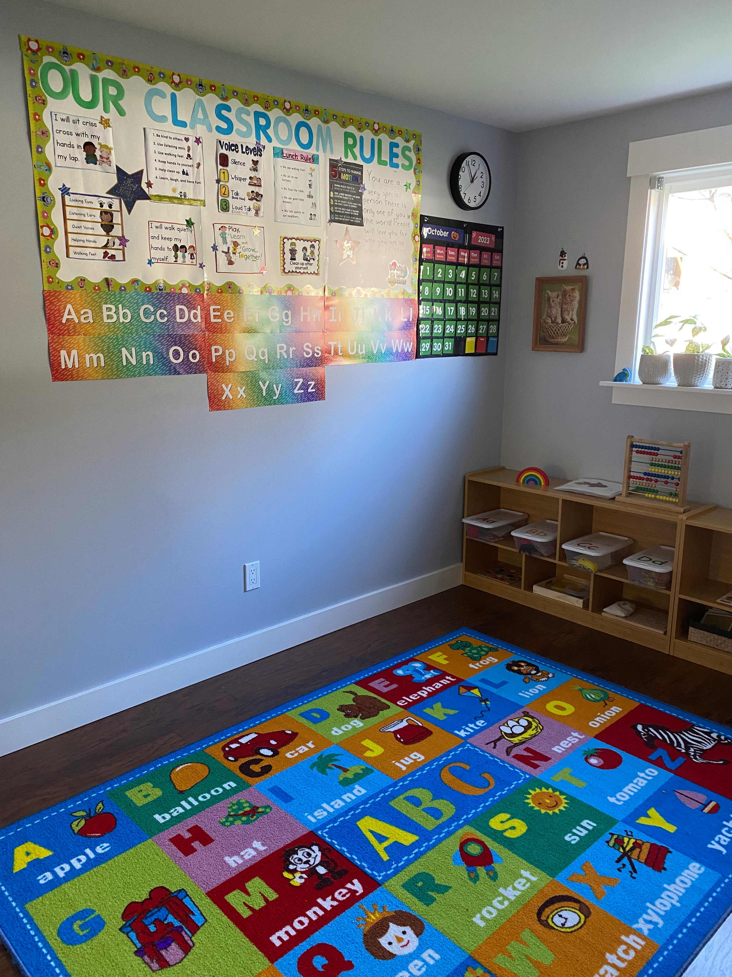 Classroom with an alphabet rug, rules poster, and shelves with learning materials