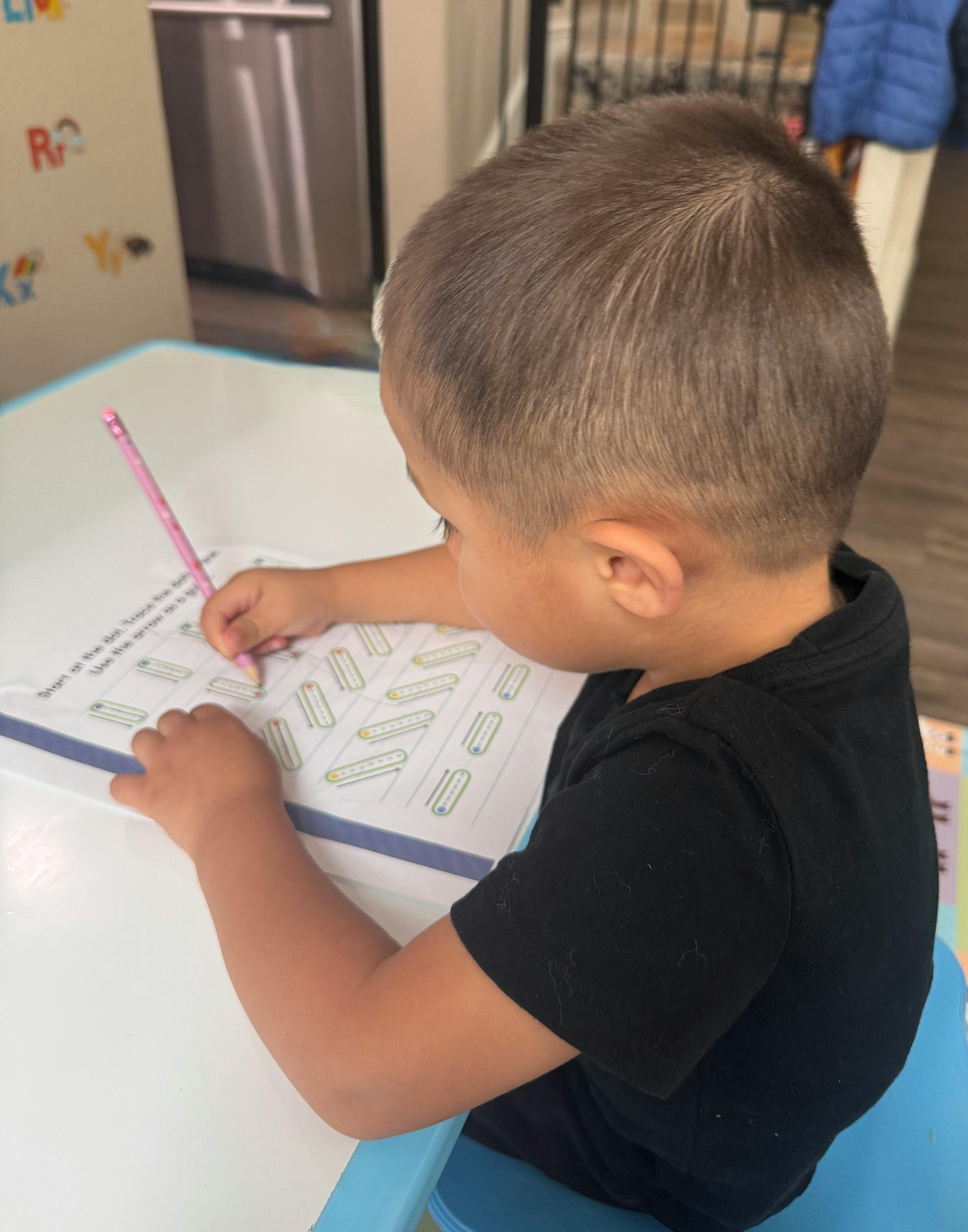 Child writing on a worksheet with a pink pencil
