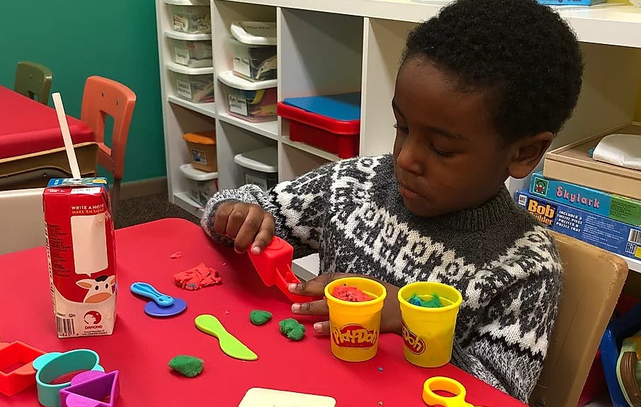 Child playing with play-doh and tools at a red table