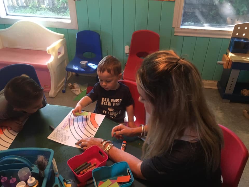 Adult and two children coloring at a table in a classroom