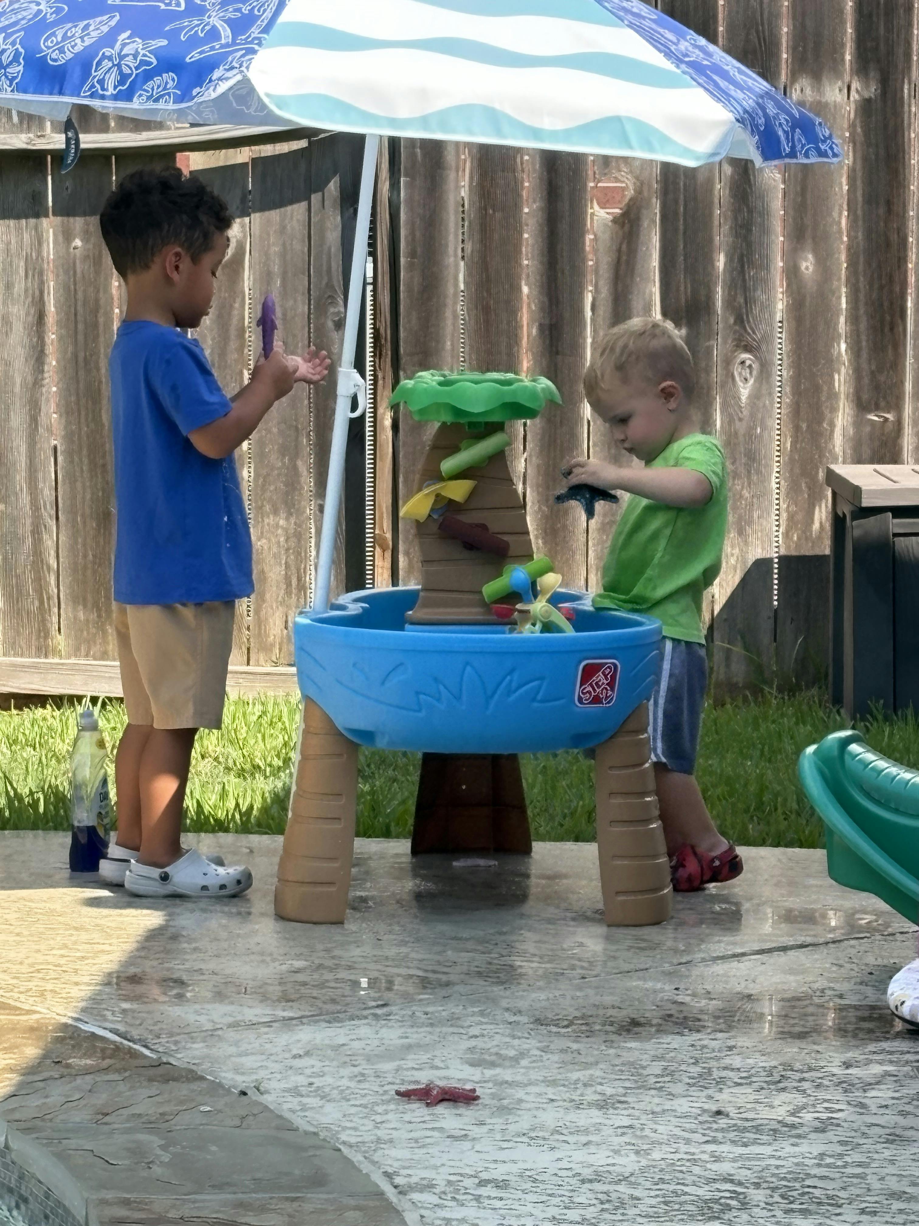 Two children playing with a water table under an umbrella