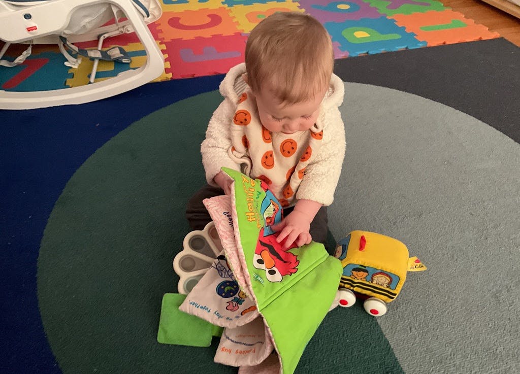 Child sitting on floor playing with a soft book and toy bus