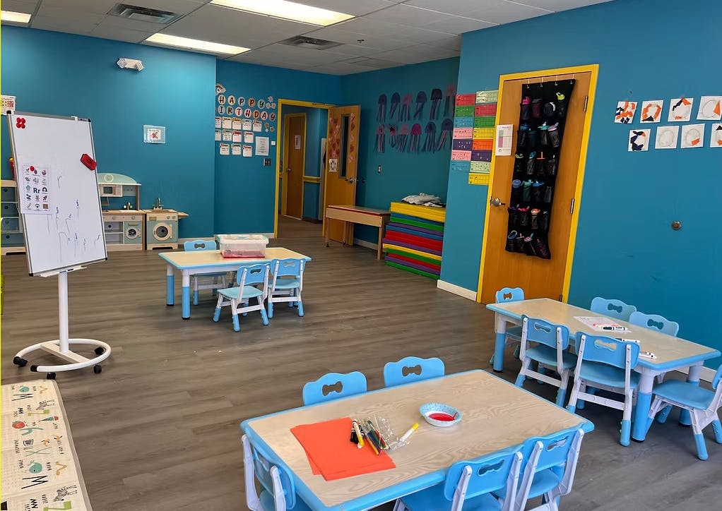 A colorful classroom with small tables and chairs, a whiteboard, and play kitchen