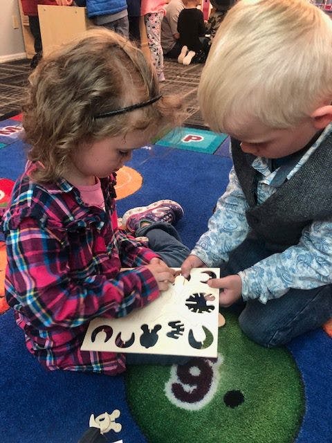 Two children playing with a puzzle on a colorful rug