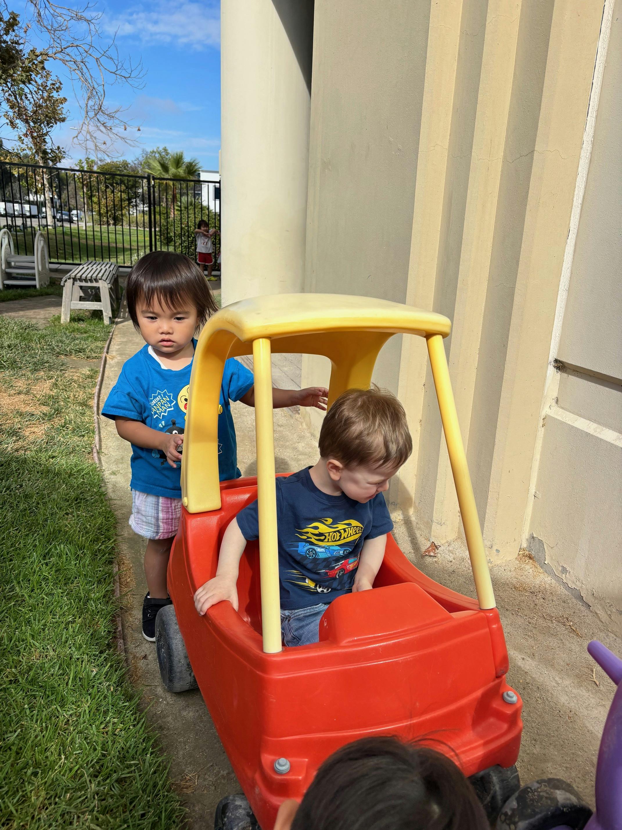 Two children playing with a red toy car outdoors