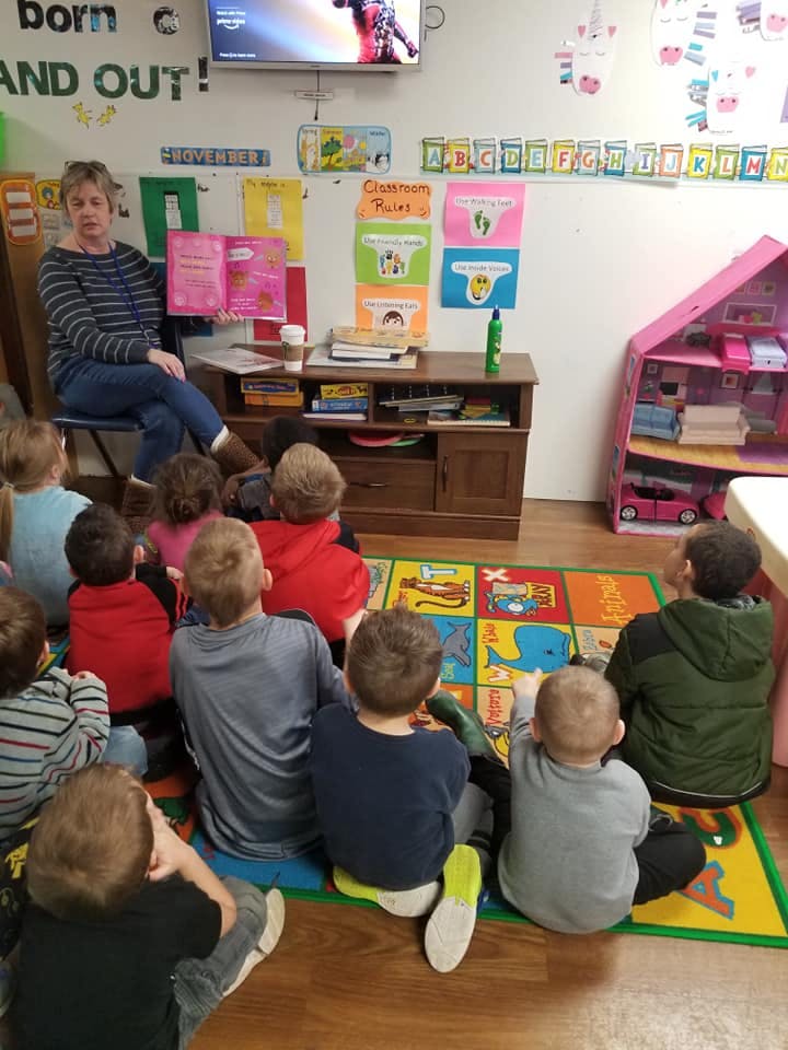 Person reading a book to a group of children sitting on a colorful rug