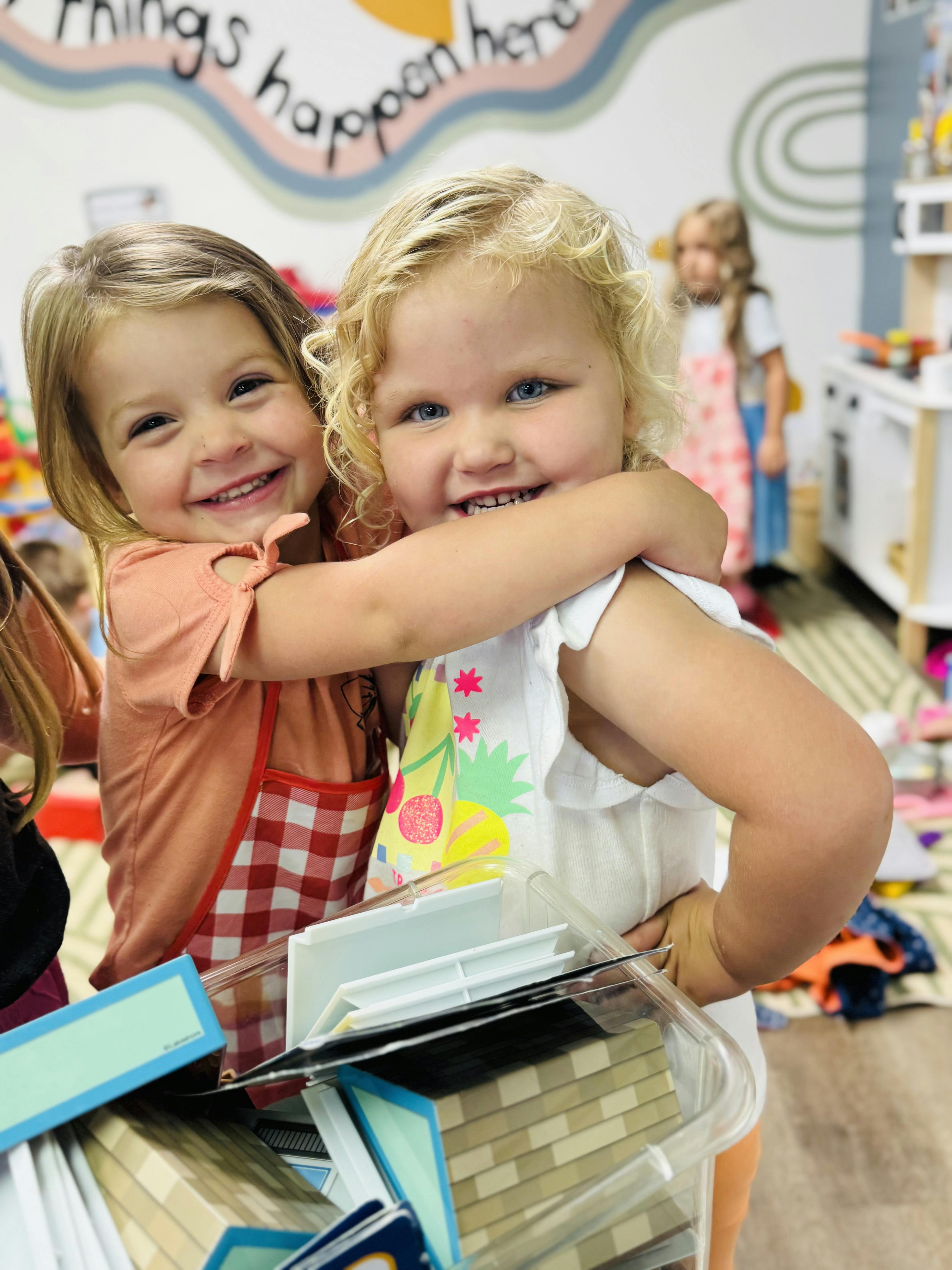 Two children smiling and hugging in a classroom