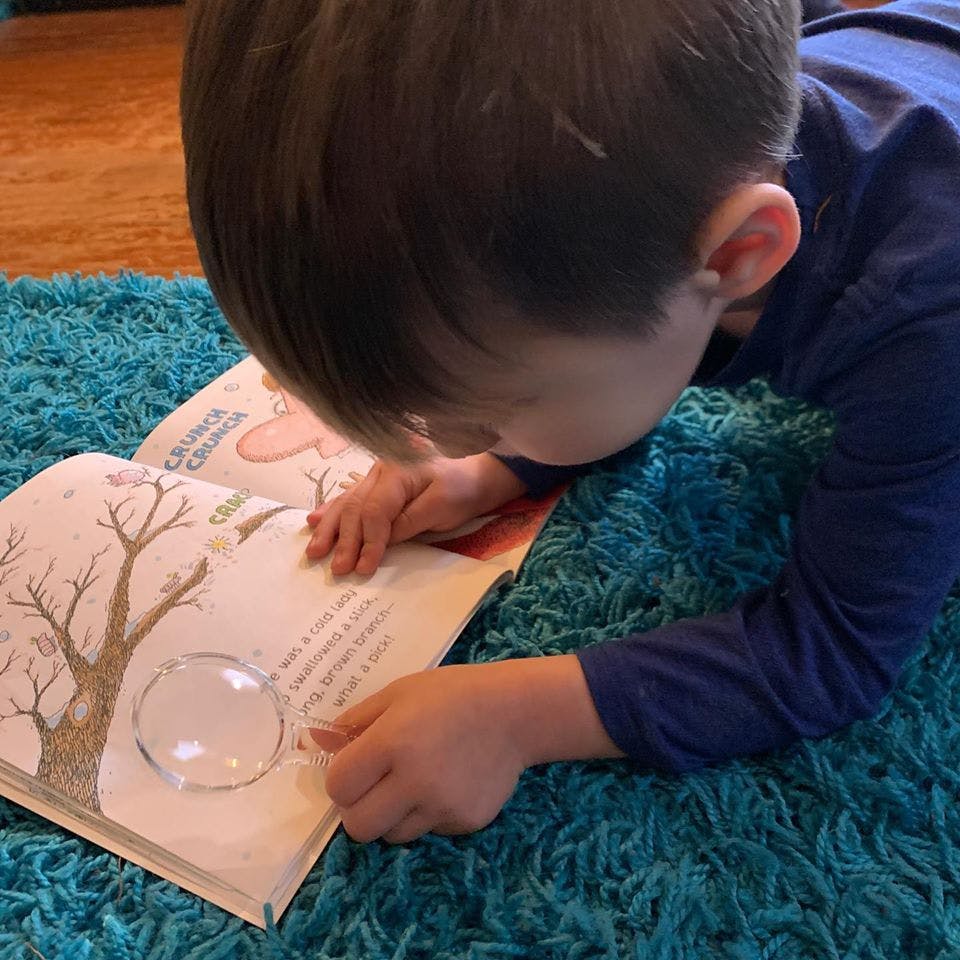 Child looking at a book with a magnifying glass