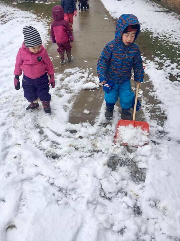 Child shoveling snow on a sidewalk with another child nearby