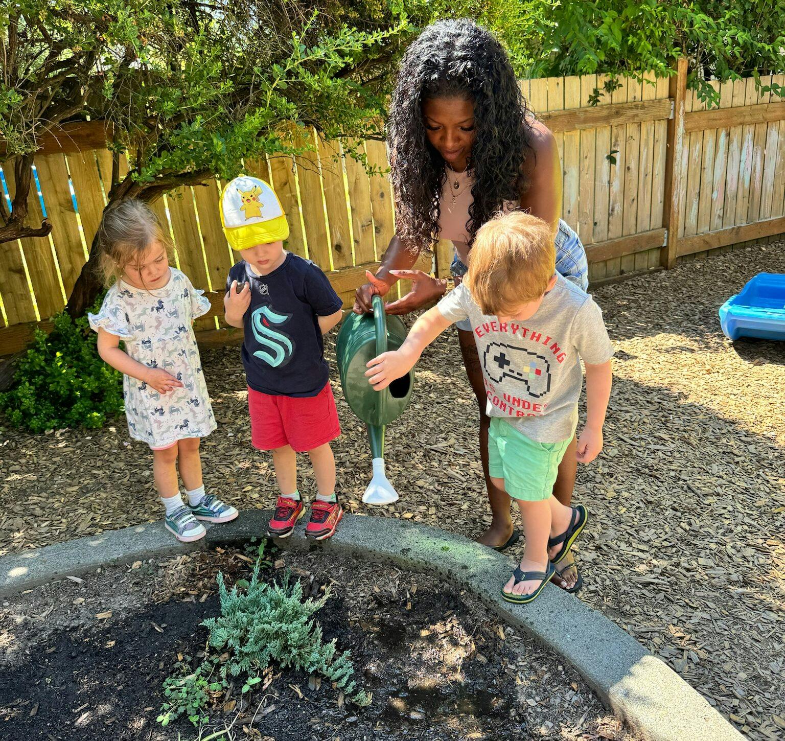 Adult and three children watering a plant in a garden bed