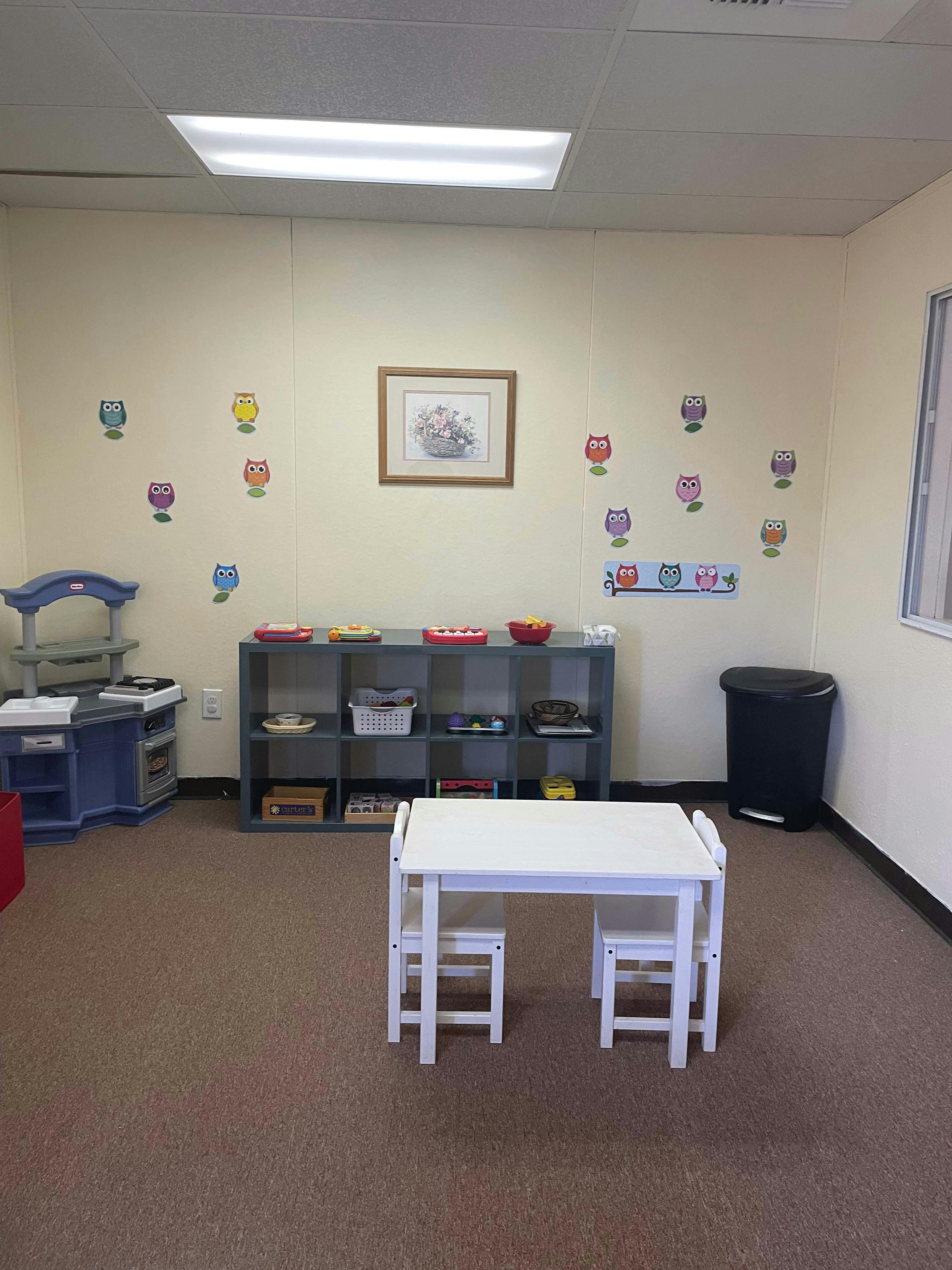 Classroom with small white table and chairs, shelves, and play kitchen