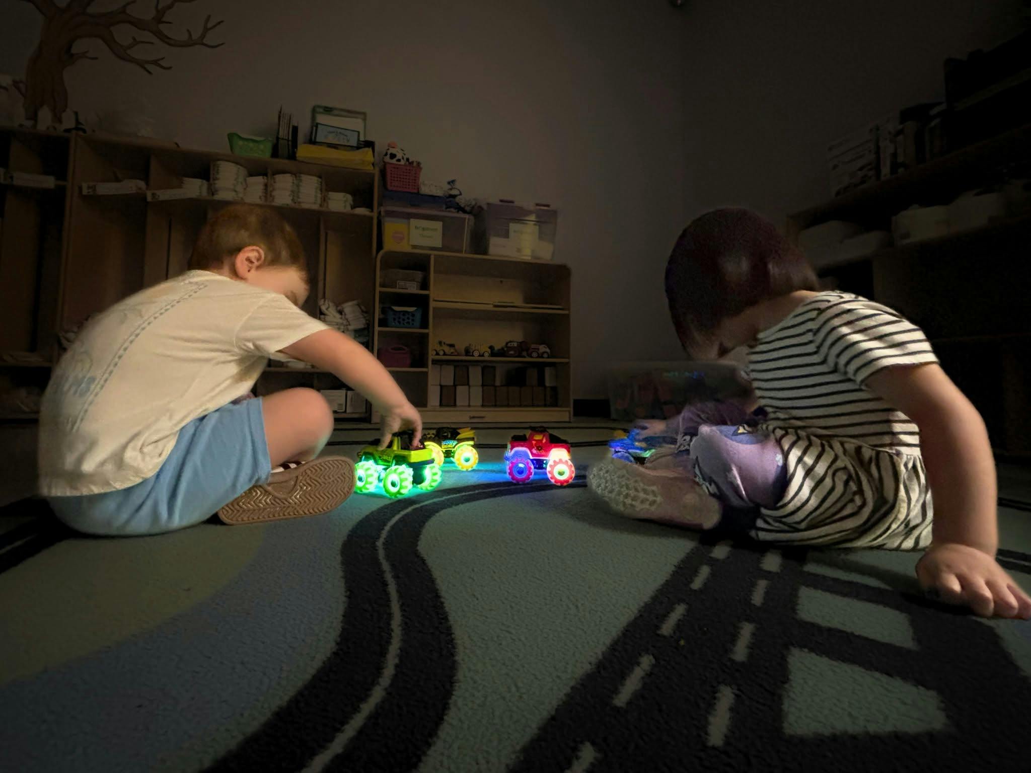 Two children sitting on a rug playing with glowing toy trucks