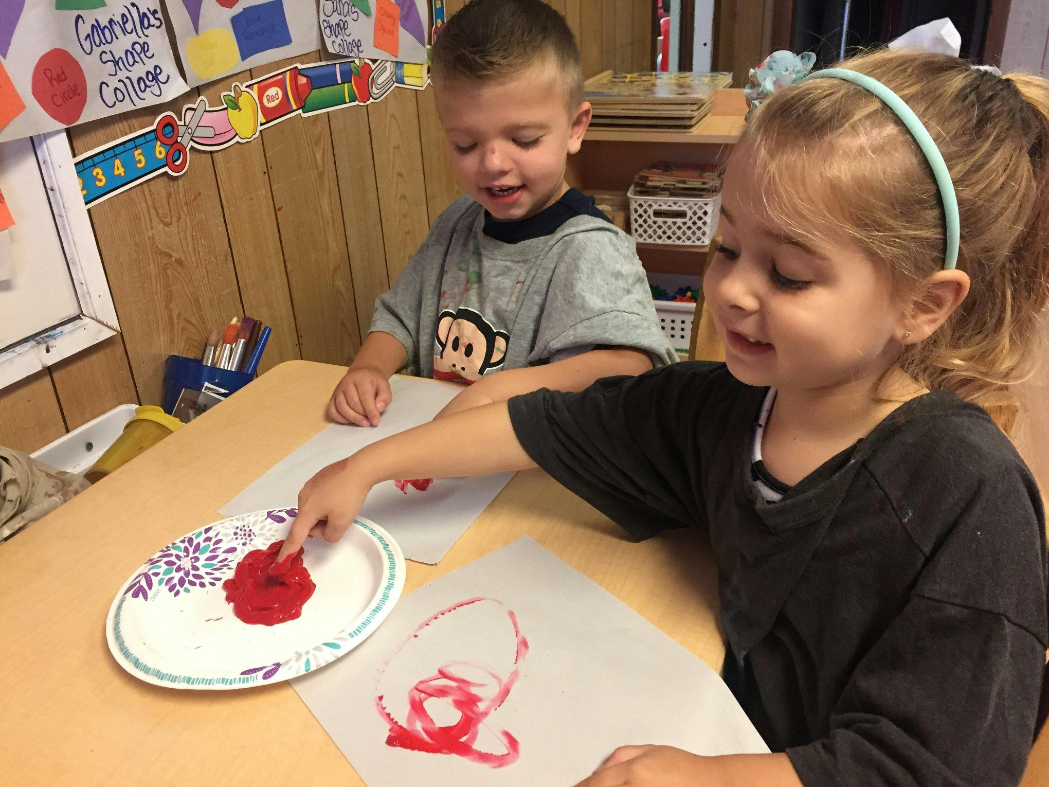 Two children finger painting at a table in a classroom