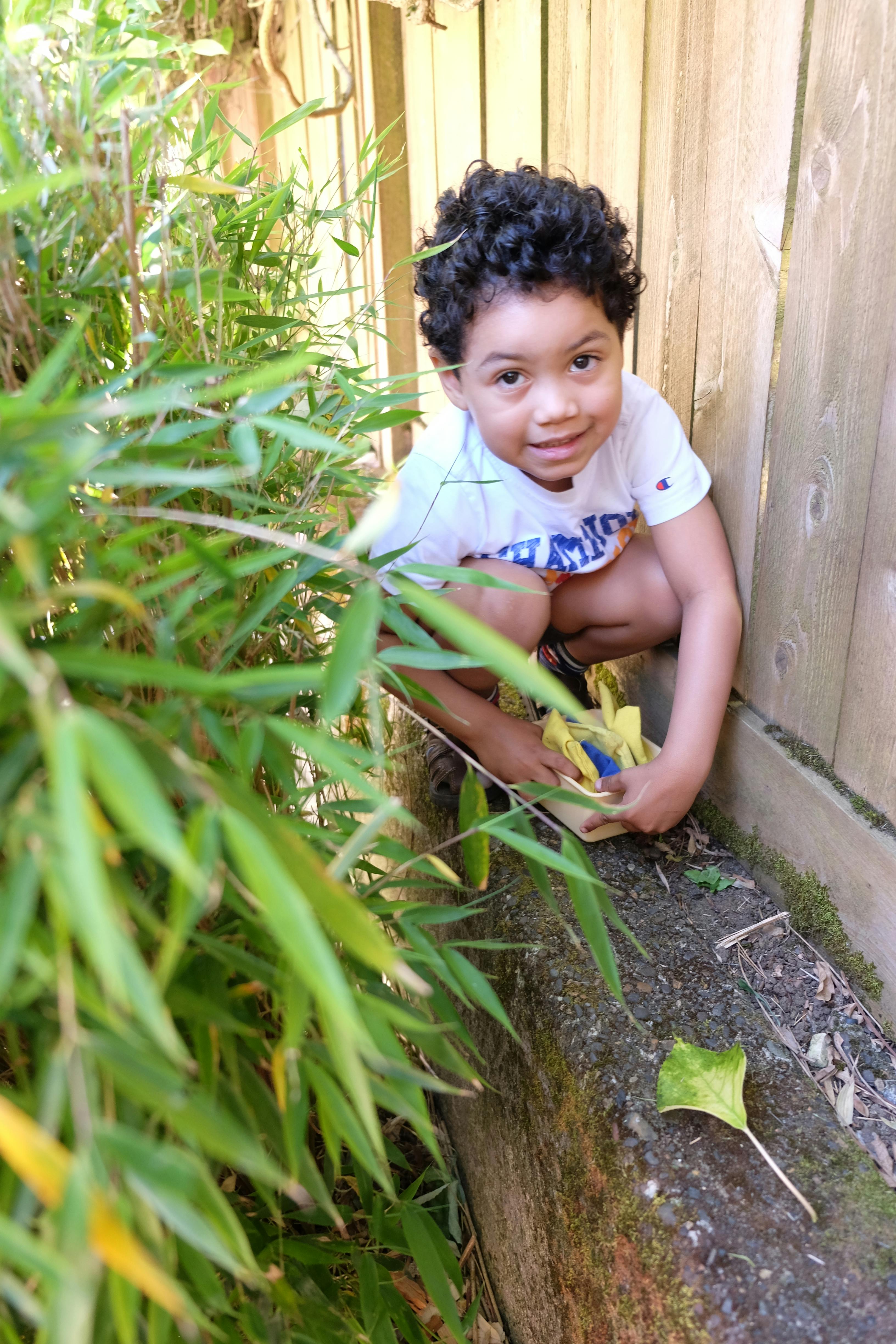 Child crouching by a wooden fence, holding an object