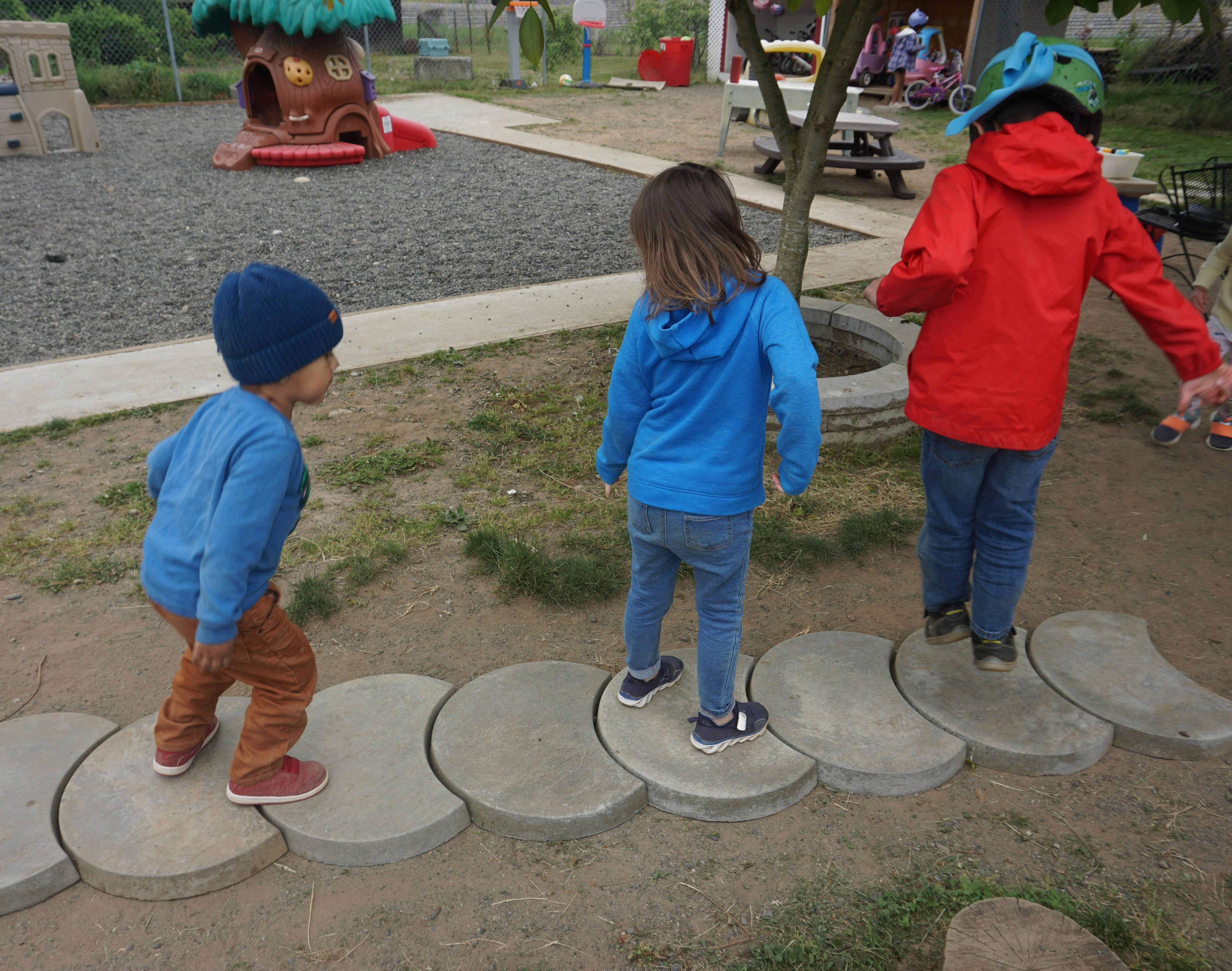 Three children walking on stepping stones on a playground