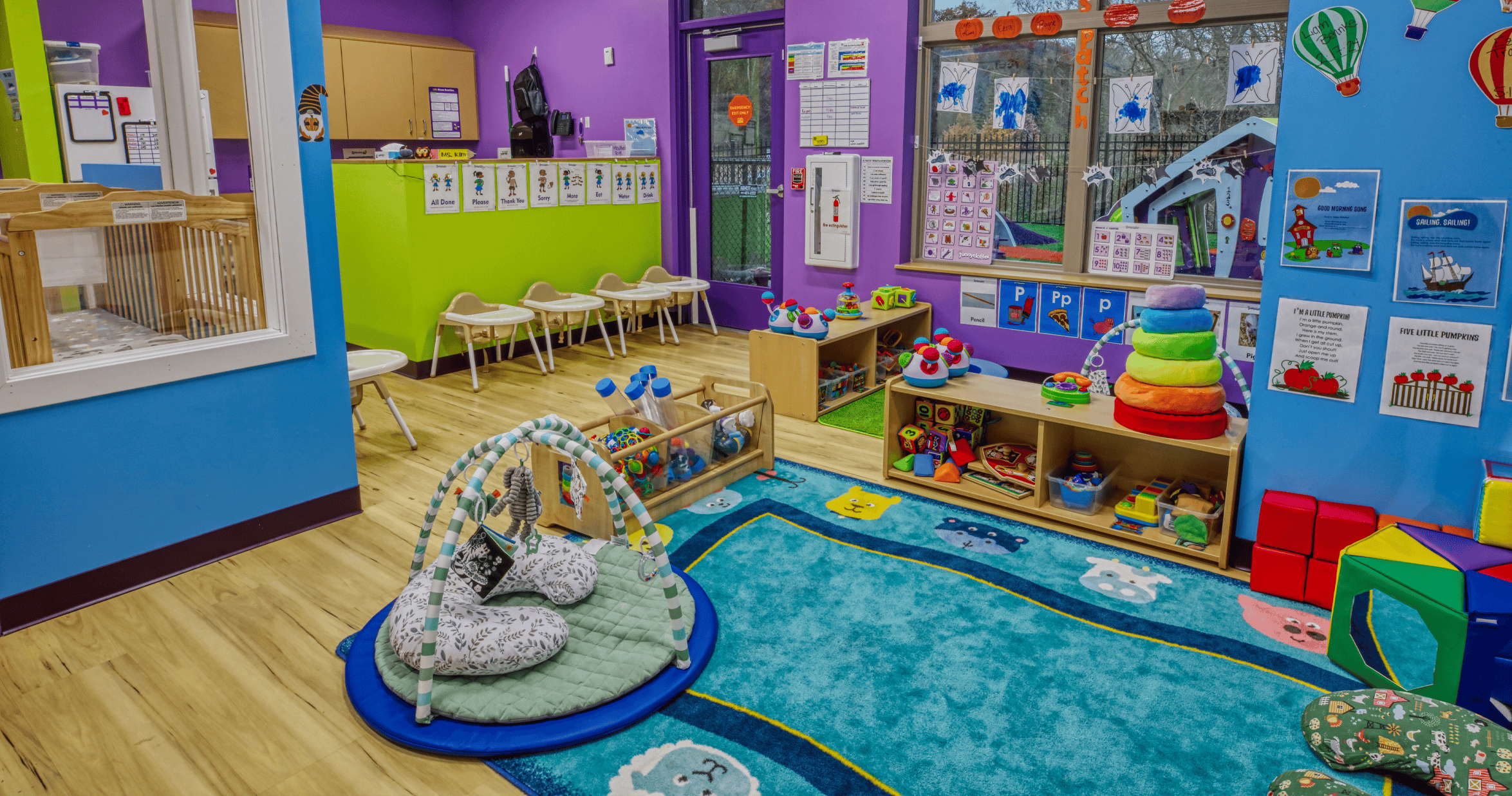 Colorful playroom with a playmat, shelves of toys, and small high chairs