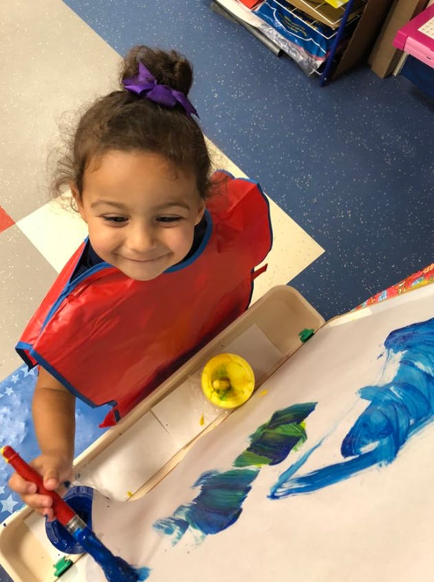 Child in a red smock painting with a brush