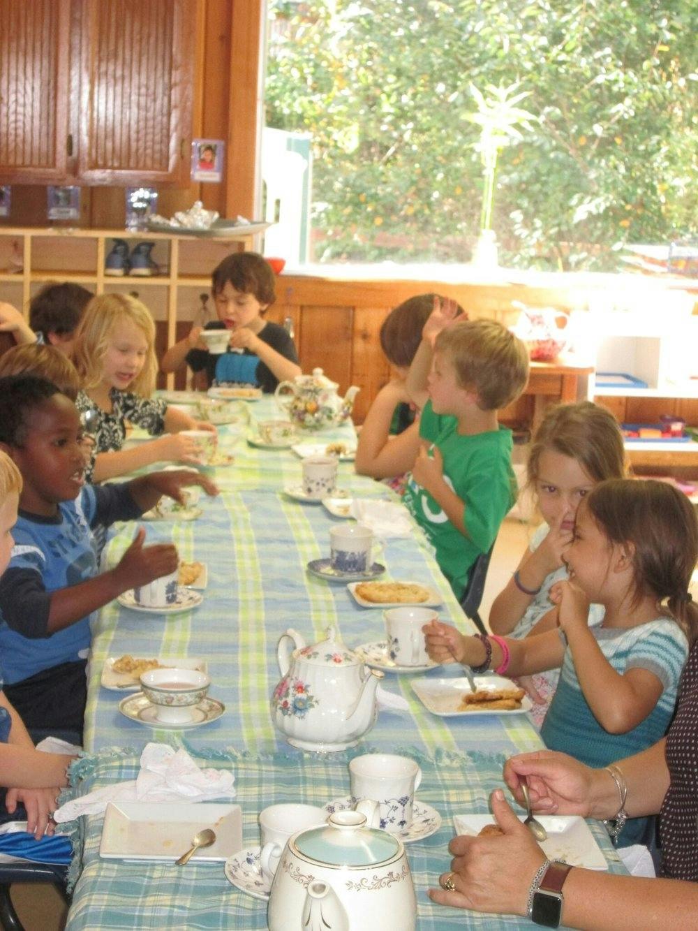 Children sitting at a long table with teacups and teapots