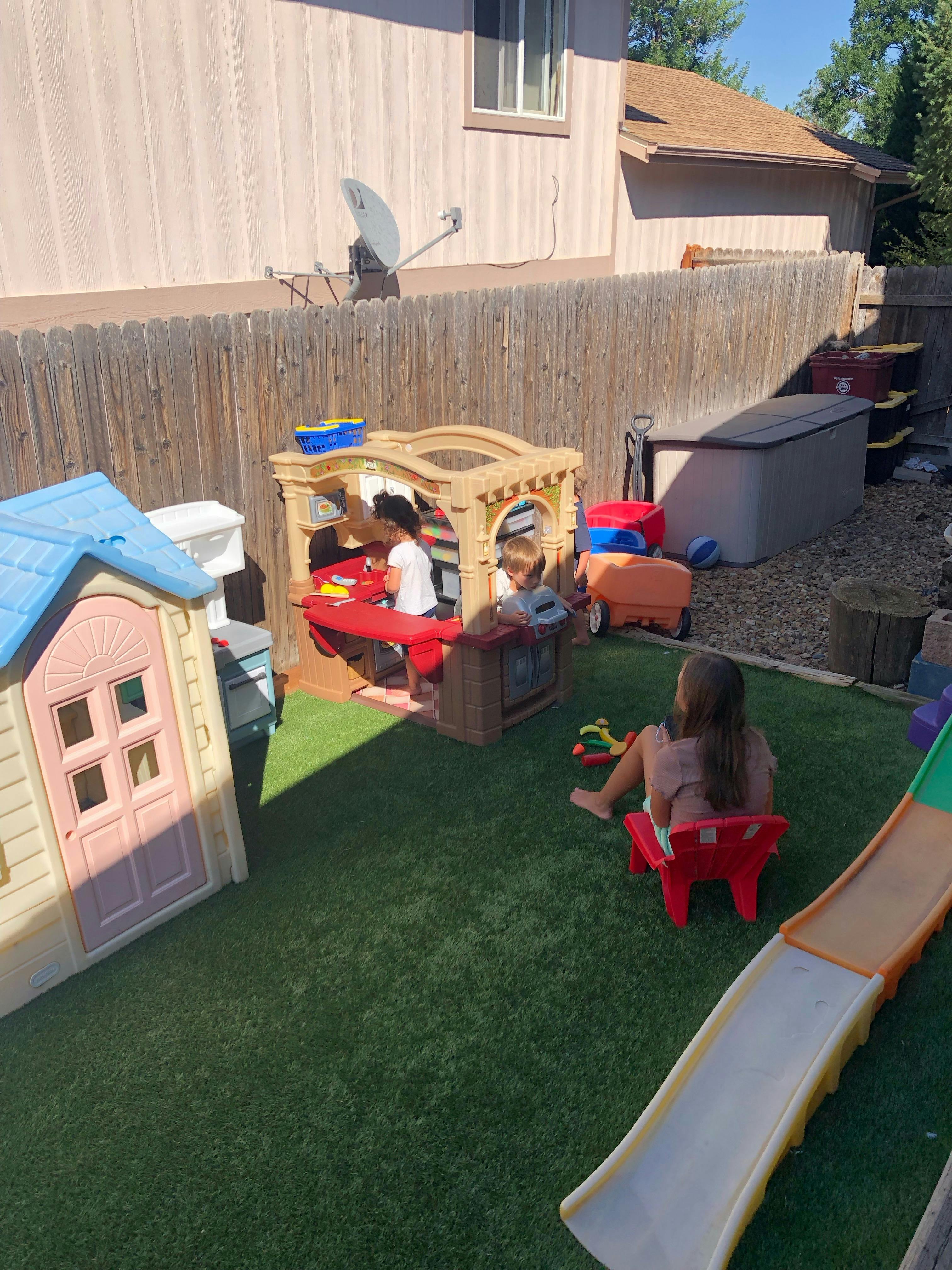 Children playing in a backyard with a playhouse and slide