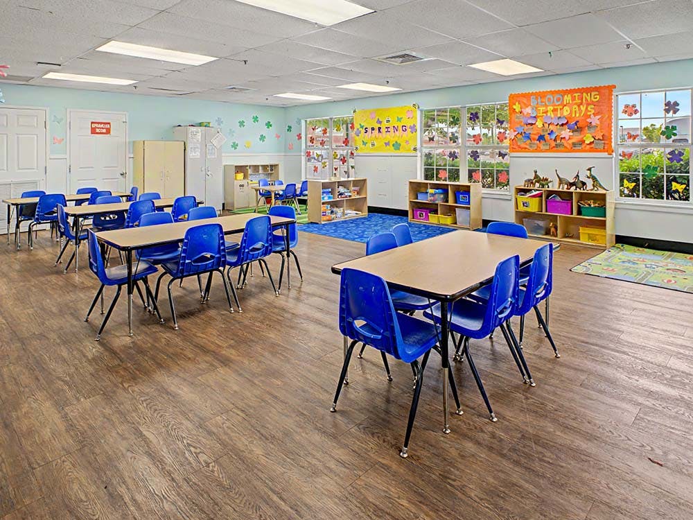 Classroom with small tables and blue chairs, educational decorations on walls and windows