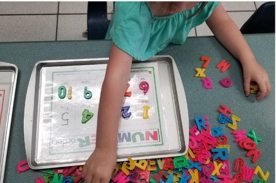 Child playing with colorful magnetic letters and numbers on a table