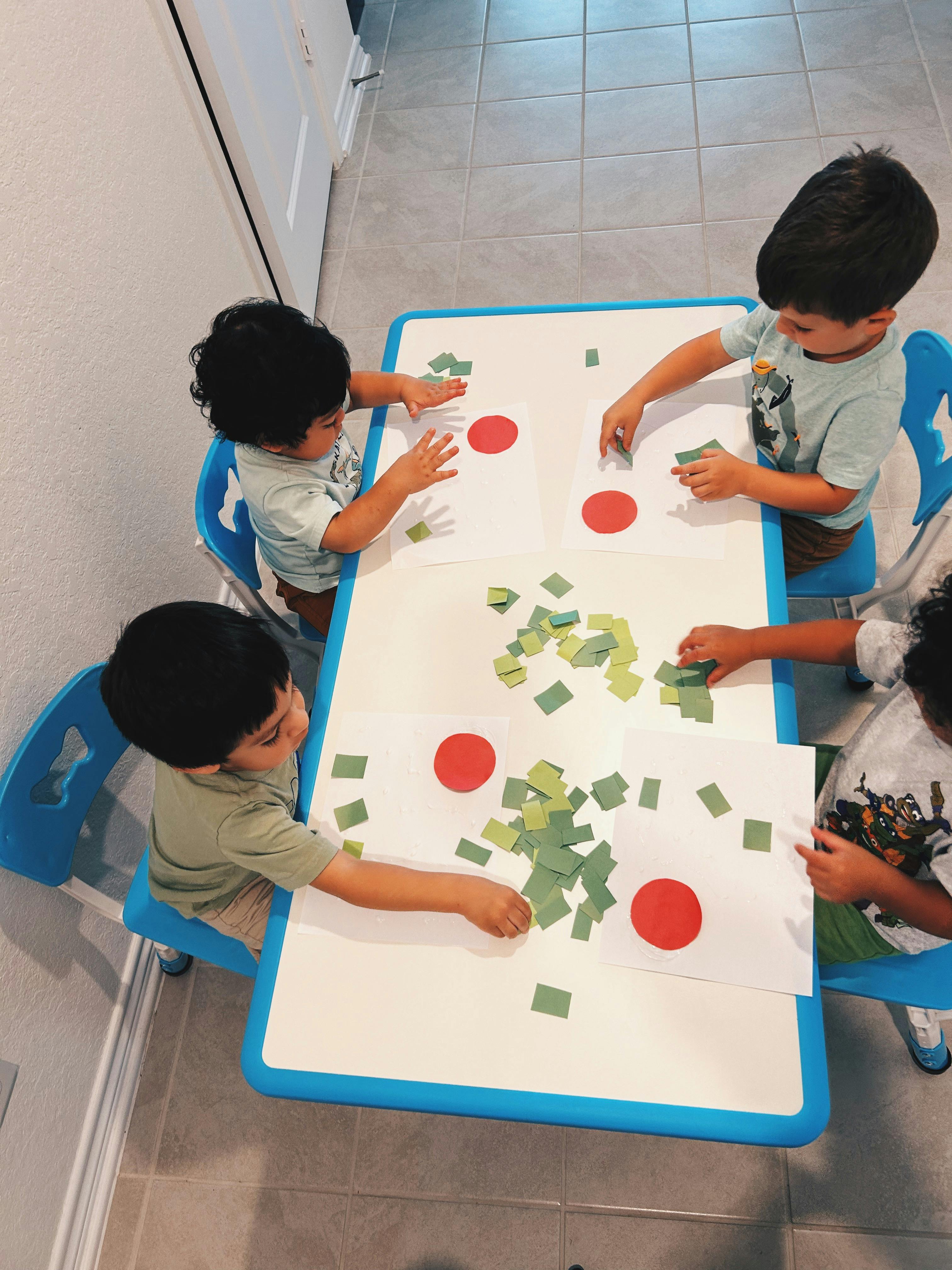 Four children at a table with paper and green squares