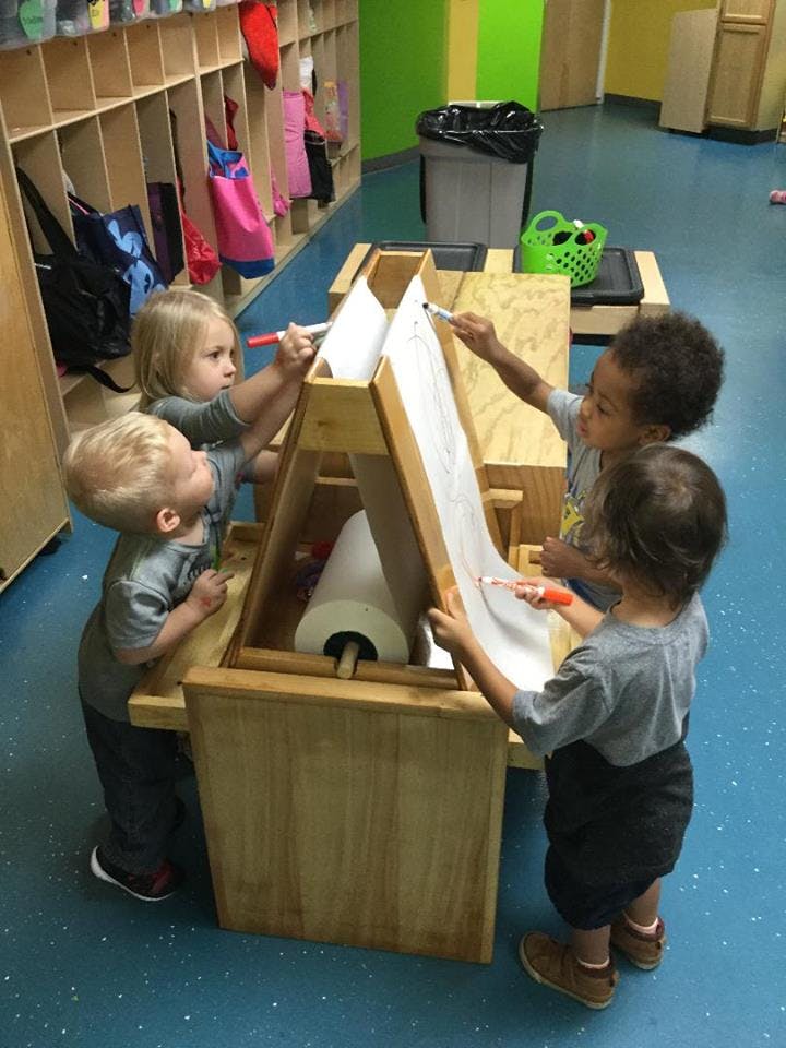 Four children drawing on an easel in a classroom