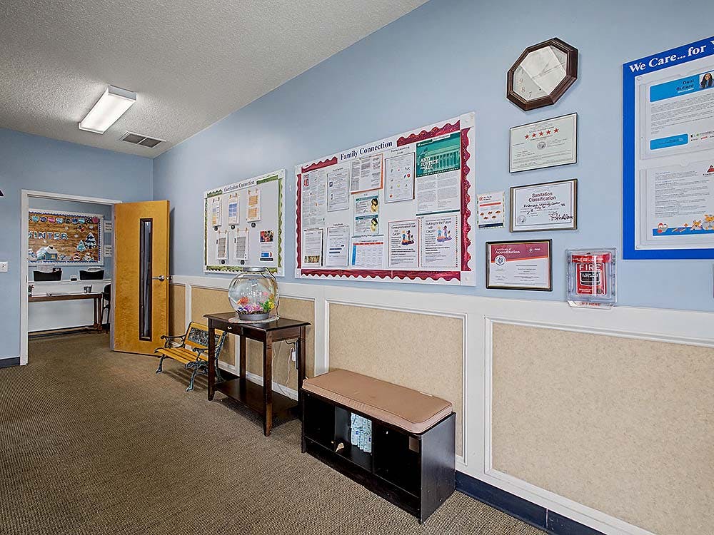 Hallway with bulletin boards, certificates on wall, a bench, and a fishbowl