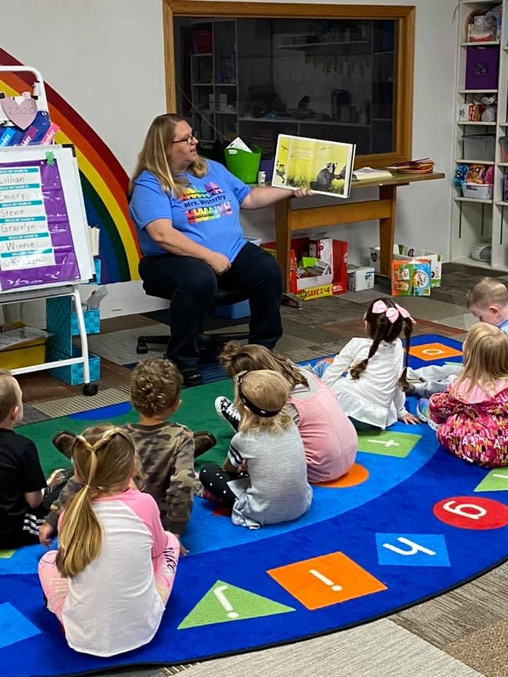 Adult reading a book to a group of children sitting on a rug