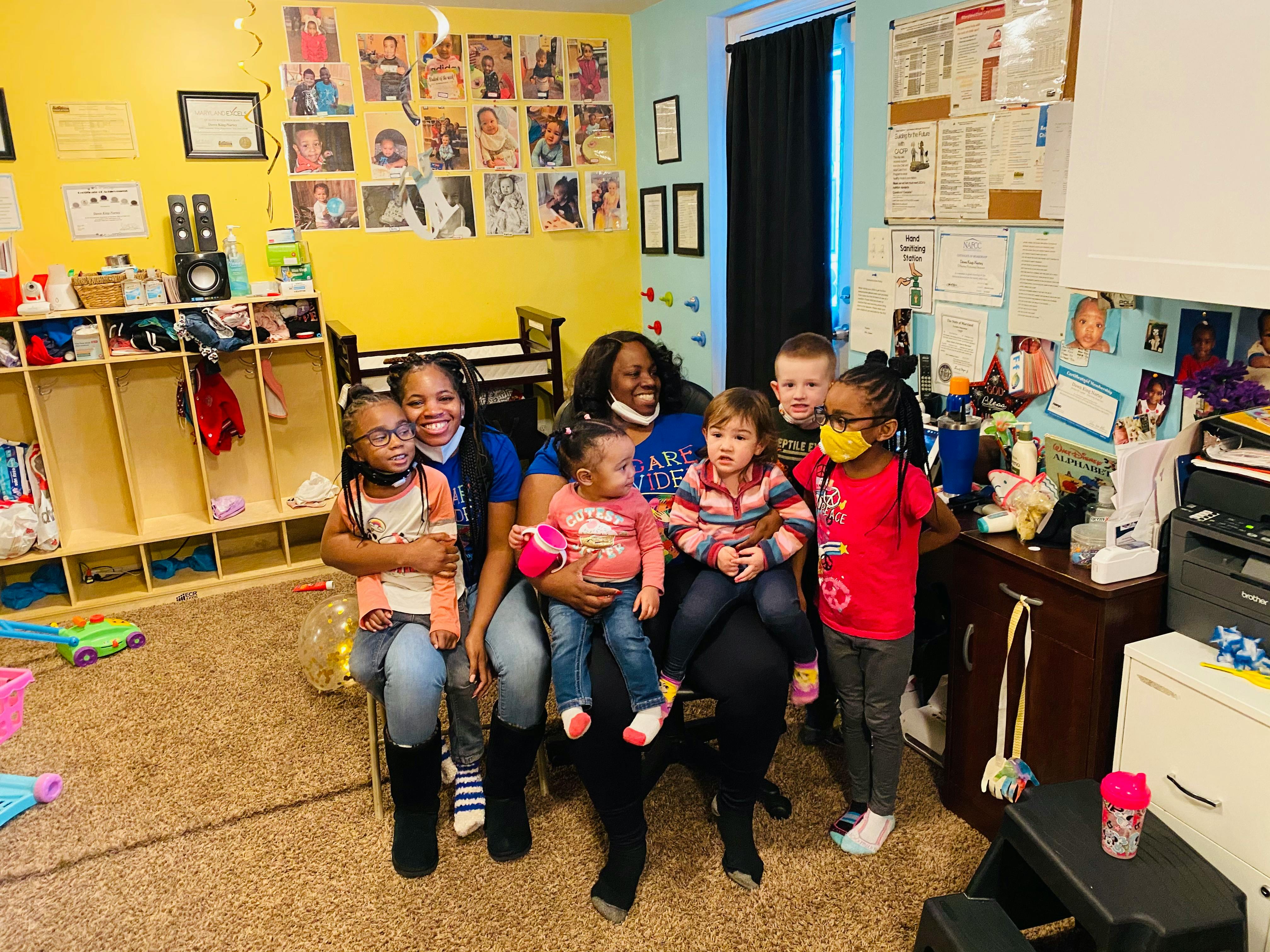 Two adults sitting with multiple children on their laps in a classroom