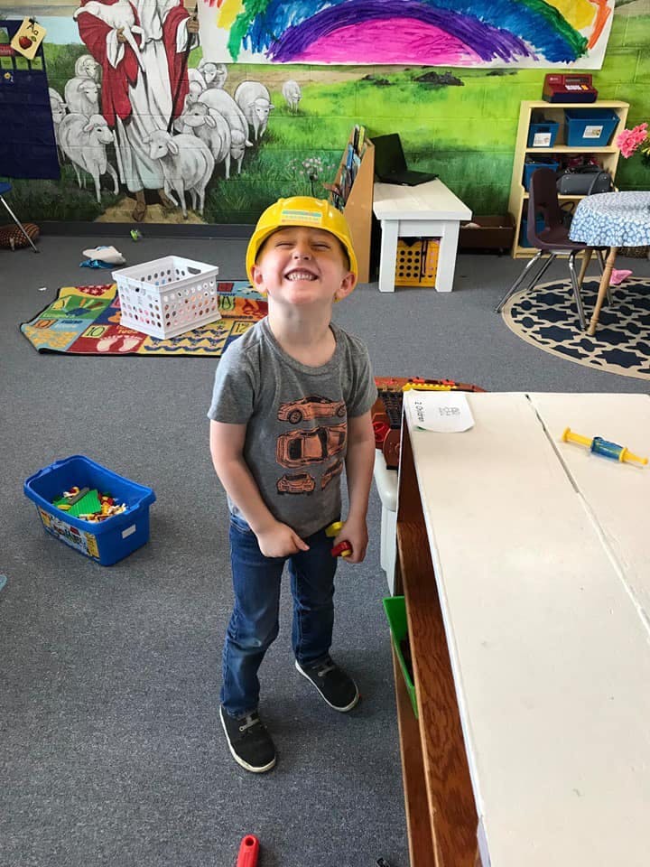 Child wearing a yellow hard hat in a classroom