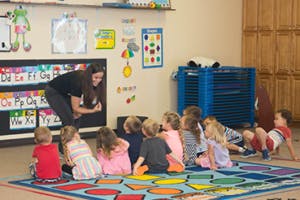 Adult interacting with children sitting on a rug in a classroom
