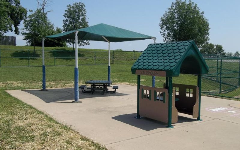 A clubhouse play structure next to a shaded picnic table in a park