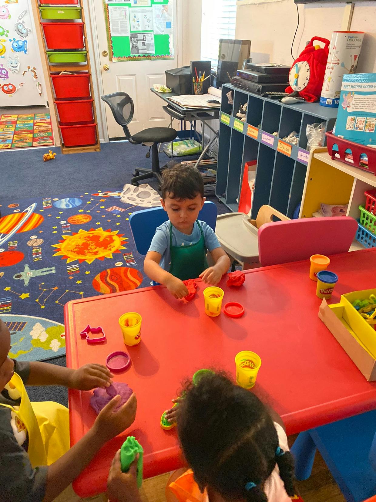 Children playing with modeling clay at a red table in a classroom