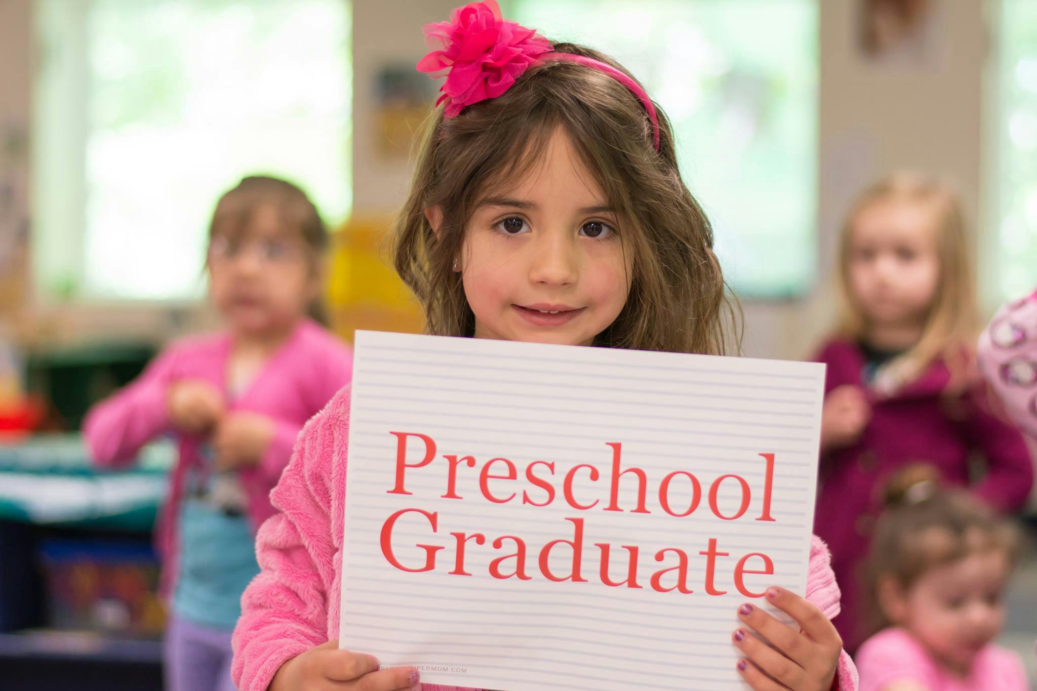 Child holding a sign that reads "Preschool Graduate"