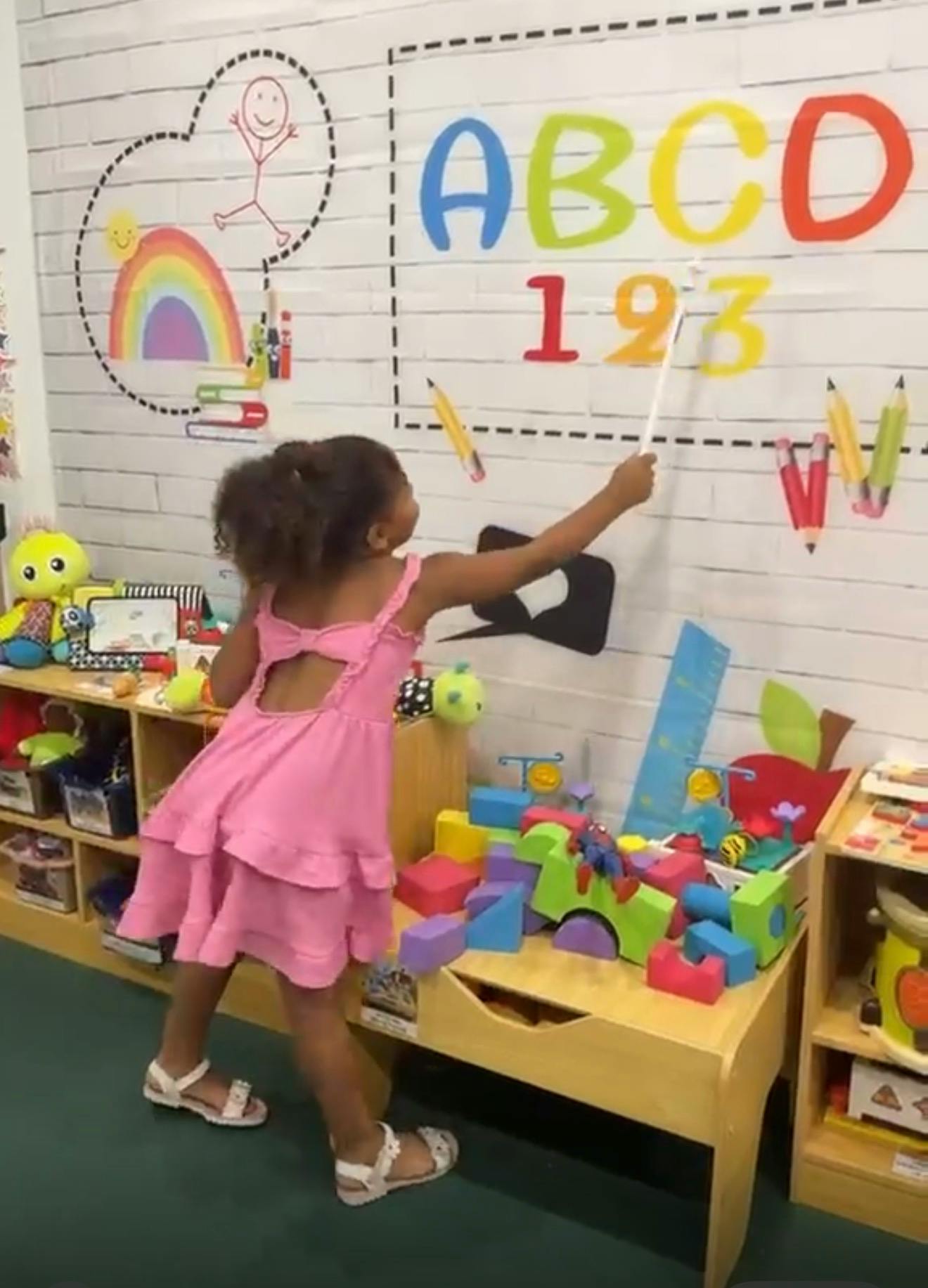 Child pointing at letters and numbers on a wall in a classroom